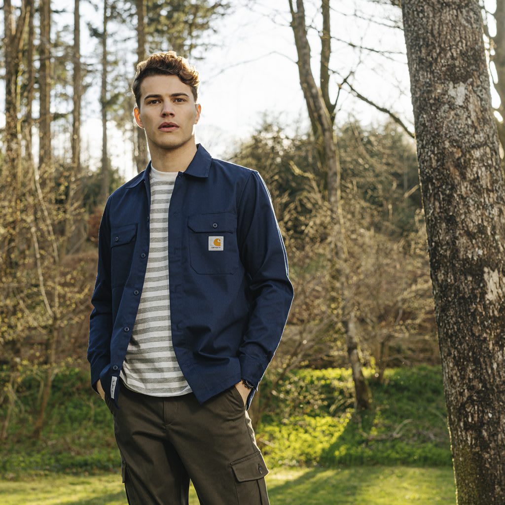 Man dressed in Carhartt stands in front of trees