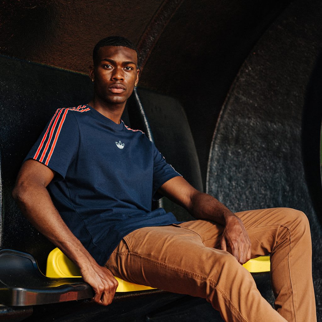 A man wearing adidas Originals sits in stadium seating