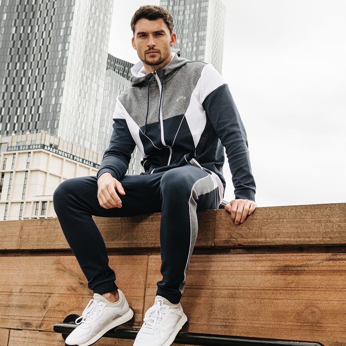 A man sitting in an urban setting wearing a BOSS Athleisure tracksuit.