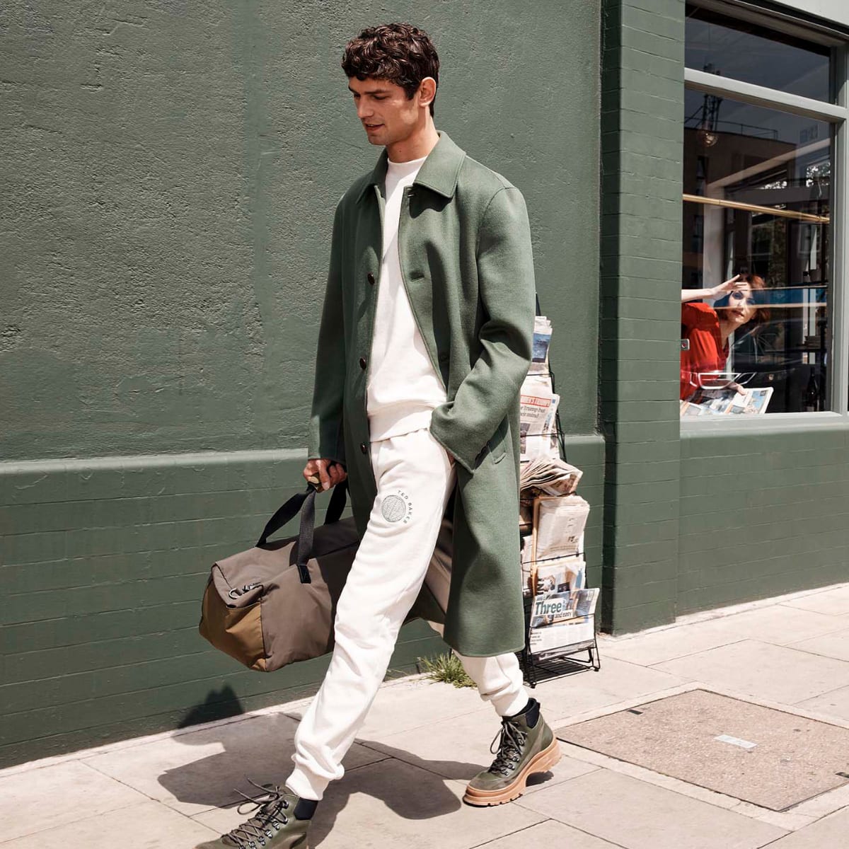 A man in white Ted Baker trousers and a long green coat walking down the street