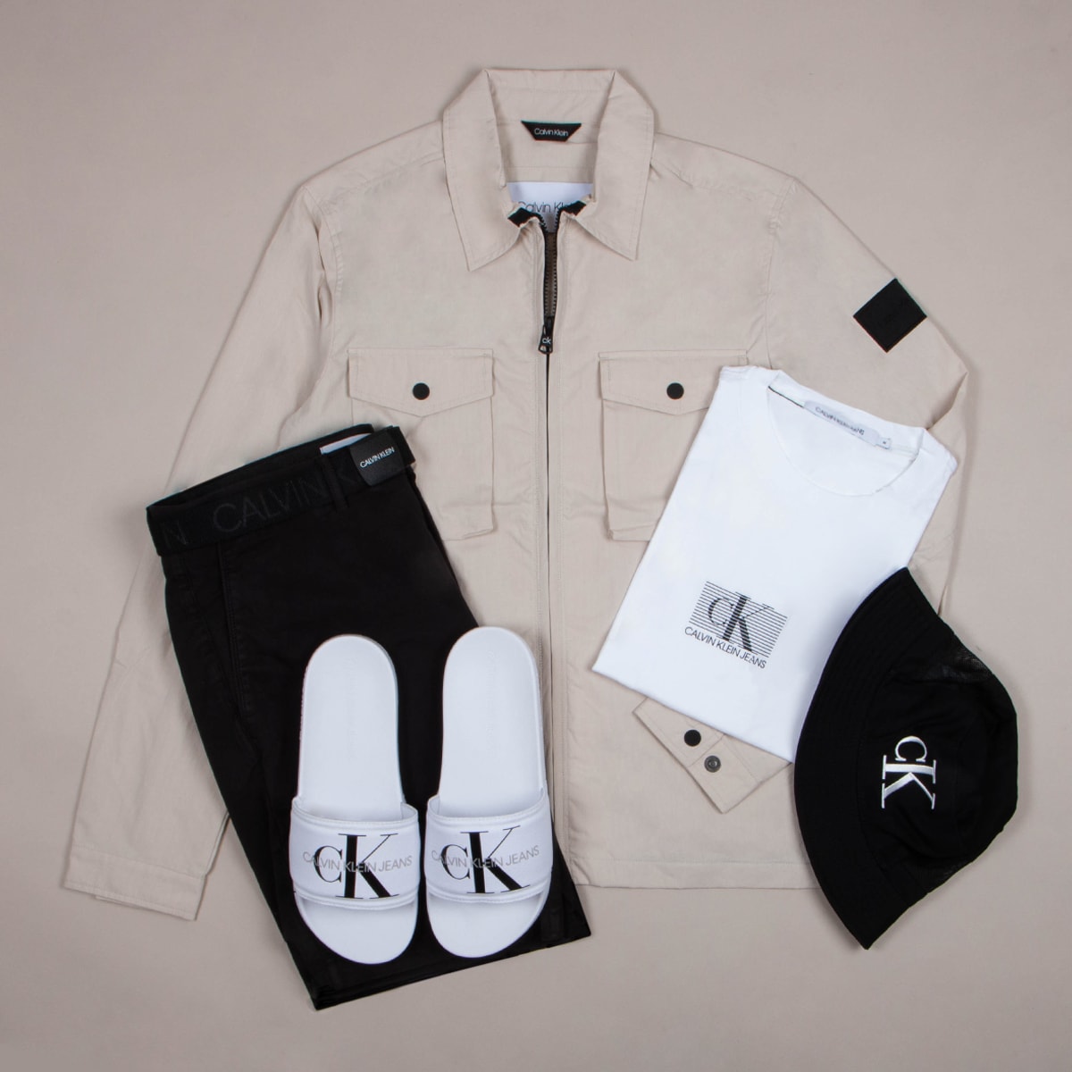 An outfit laid out including a jacket, slides, a T shirt and a hat