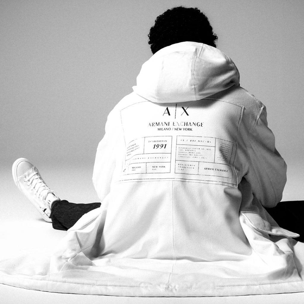 A man sitting on the floor looking away from the camera wearing a white hoodie by Armani Exchange