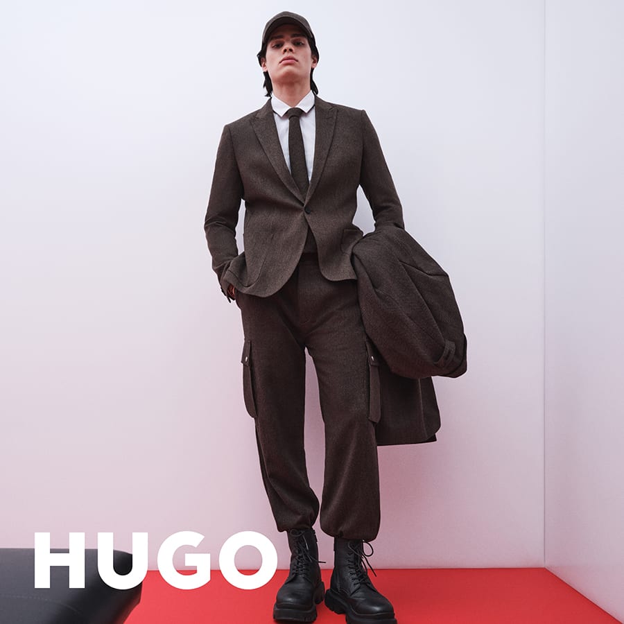 A man leaning against a wall dressed in a HUGO suit
