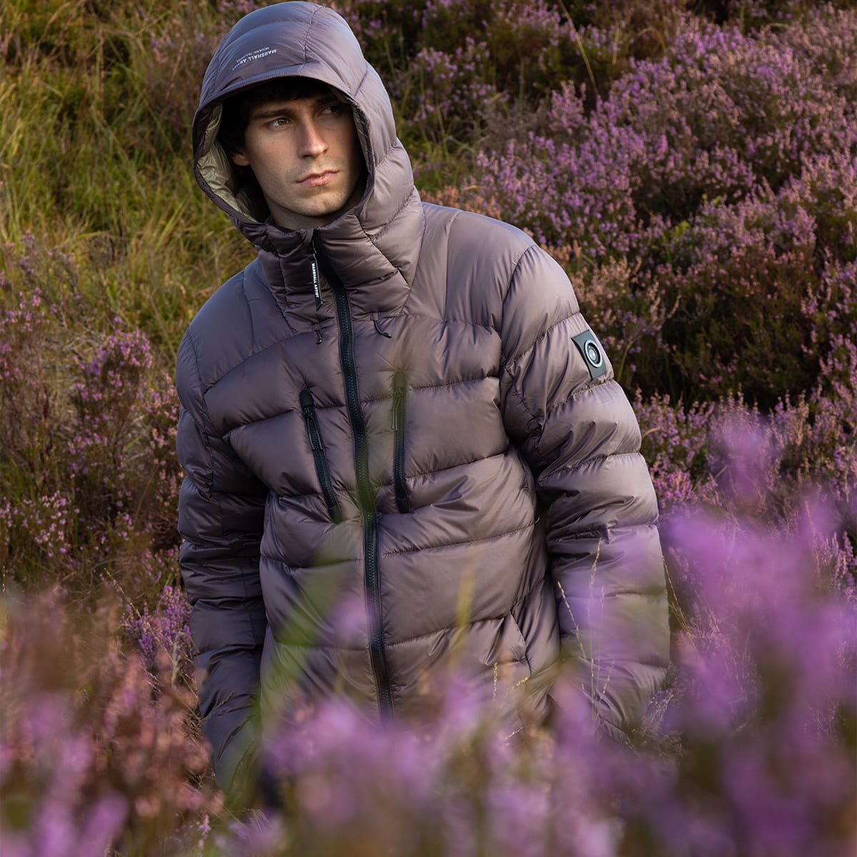 A man dressed in a Marshall Artist jacket with the hood up