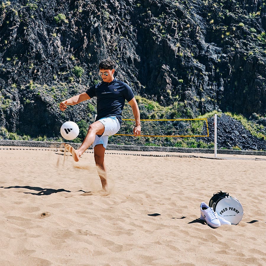 A man wearing Fred Perry playing football on the beach