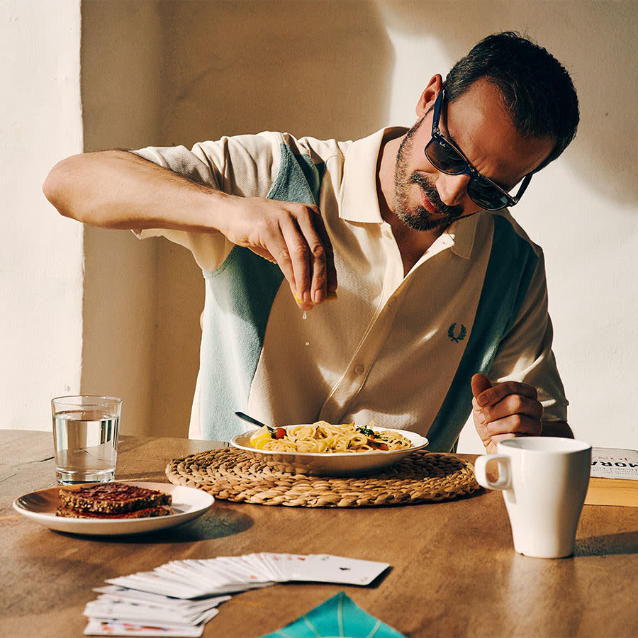 A man dressed in Fred Perry squeezes lemon over pasta