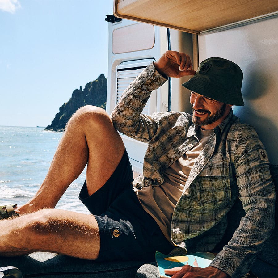 A man in Belstaff clothes sitting in a campervan by the sea