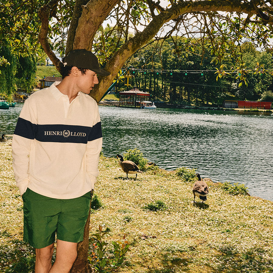 A man wearing Henri Lloyd clothes stands under a tree by some geese