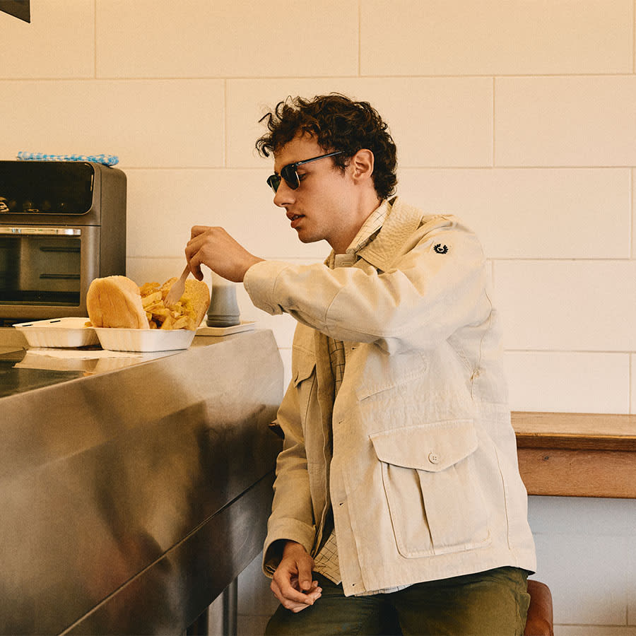 A man in a Belstaff jacket tucking into a chip butty
