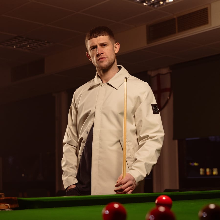 A man wearing a Marshall Artist jacket and holding a pool cue