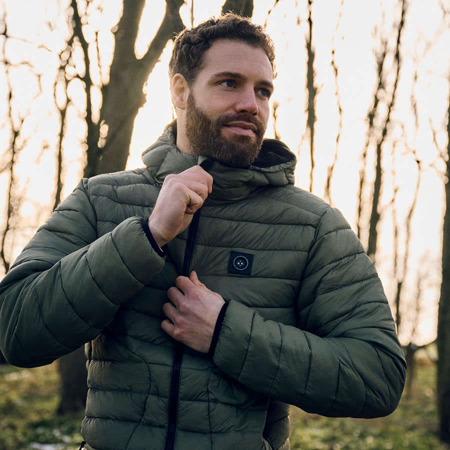 A man zipping up his jacket in a forest