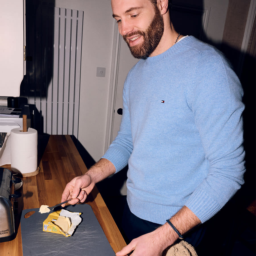 A man wearing a blue jumper is cooking in the kitchen