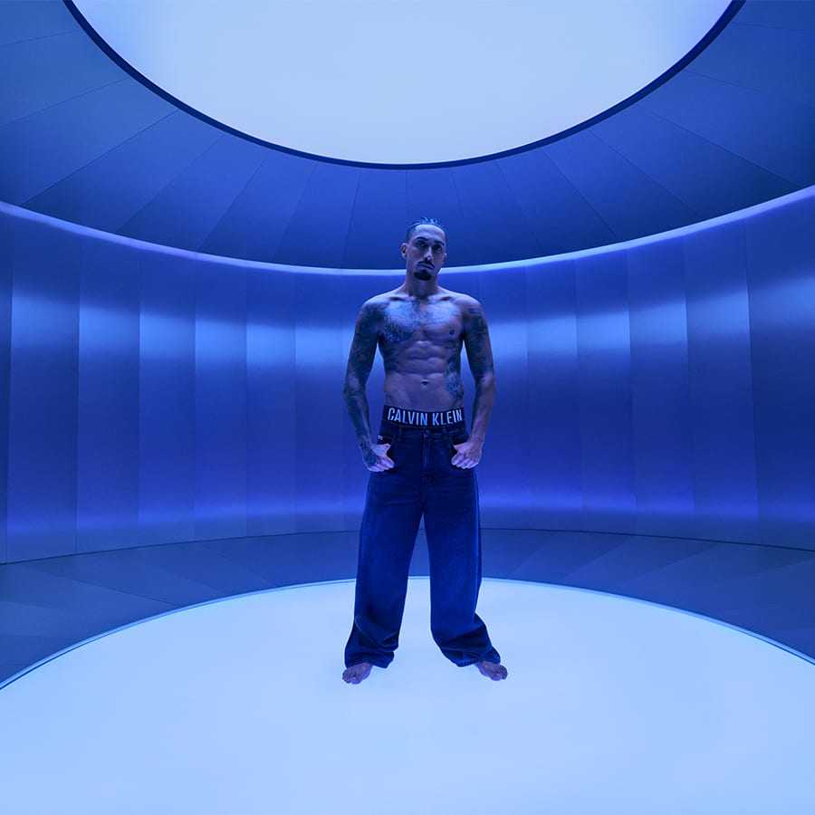 A man dressed in Calvin Klein jeans standing in a blue room