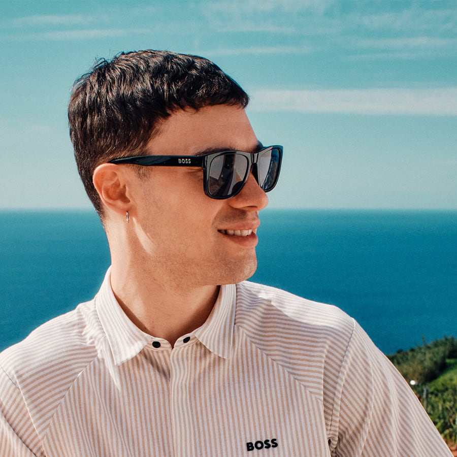 A man wearing a BOSS shirt and sunglasses by the sea