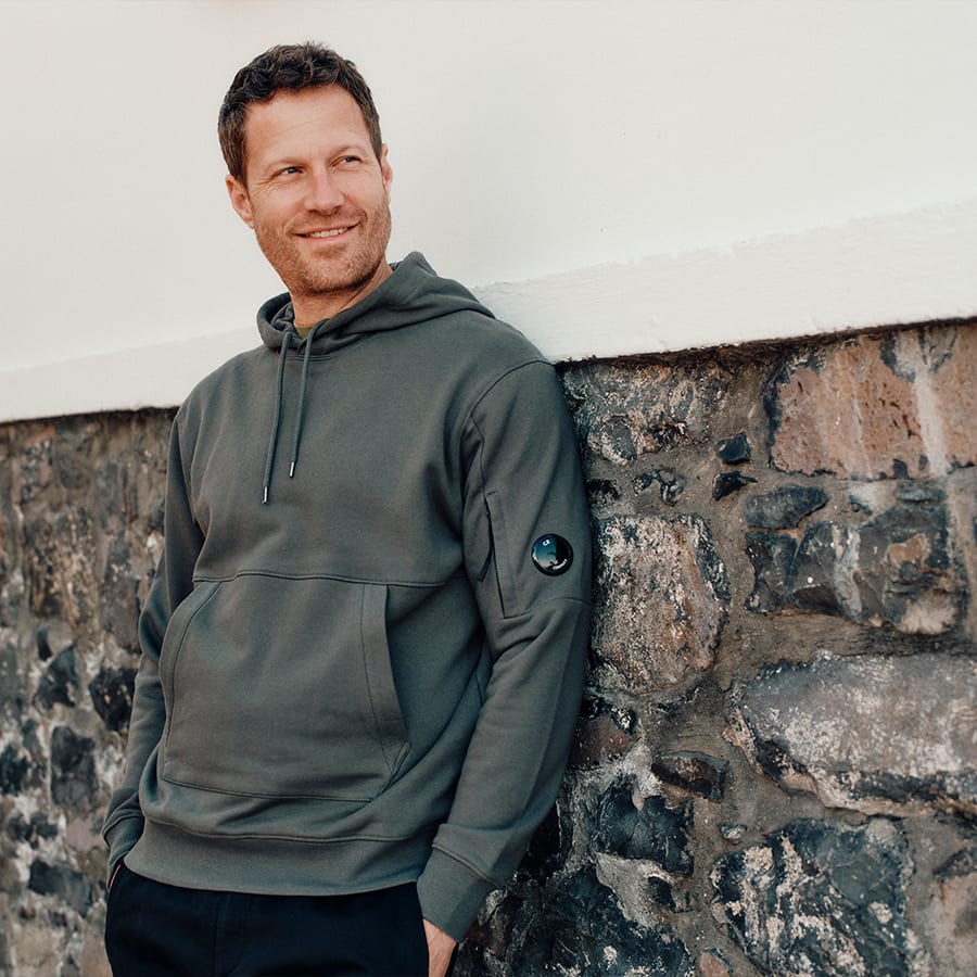 A man leaning against a wall, wearing a grey jacket