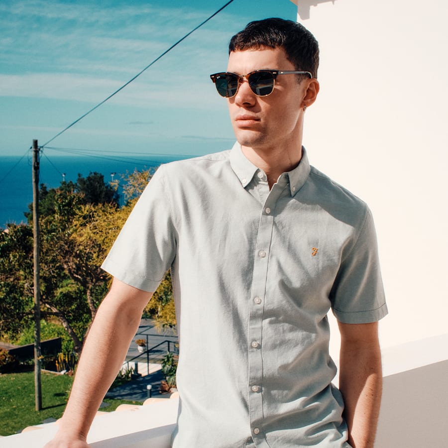 A man leaning on a wall wearing a short sleeved shirt