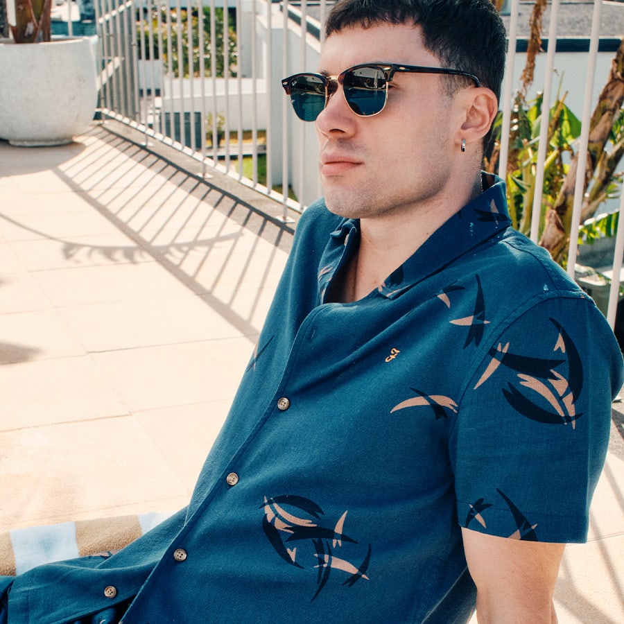 A man wearing a blue short-sleeved shirt sitting in the sun.