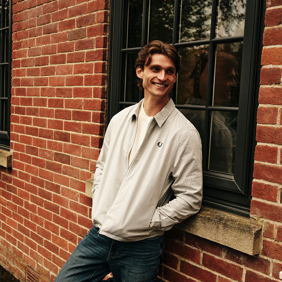 A smiling man leans against a building