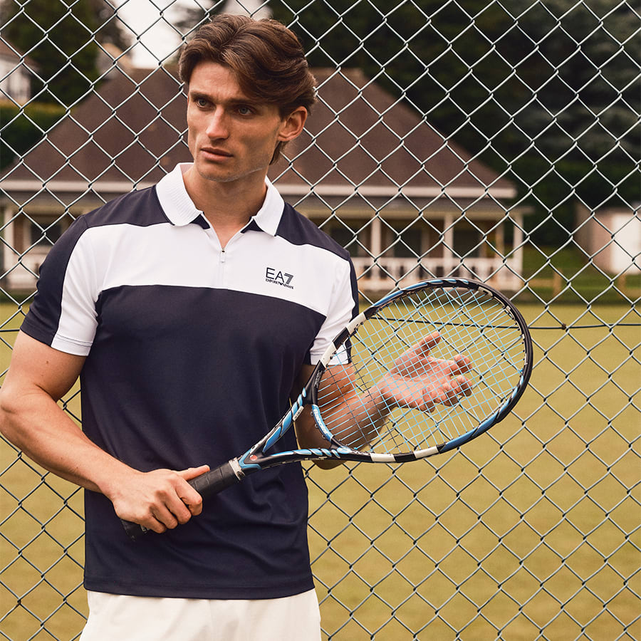 A man wearing an EA7 polo shirt holding a tennis racket