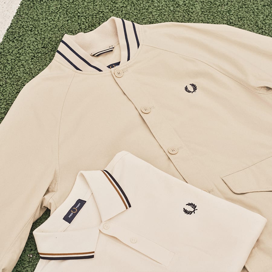 A Fred Perry polo shirt and jacket laid out on a tennis court