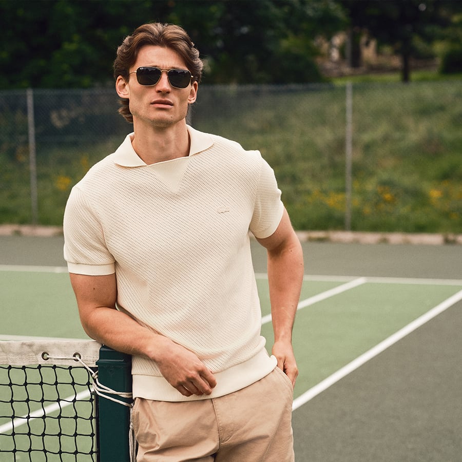 A man leaning against a tennis net wearing Lacoste