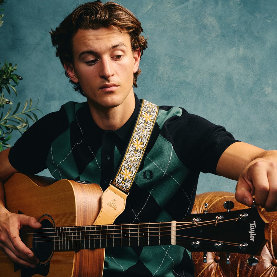 A man wearing Fred Perry tuning a guitar