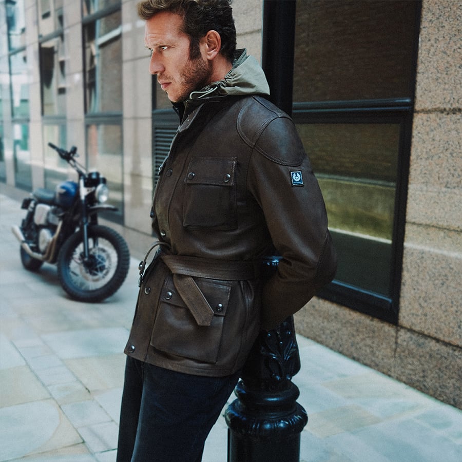 A man leaning on a post wearing a Belstaff jacket