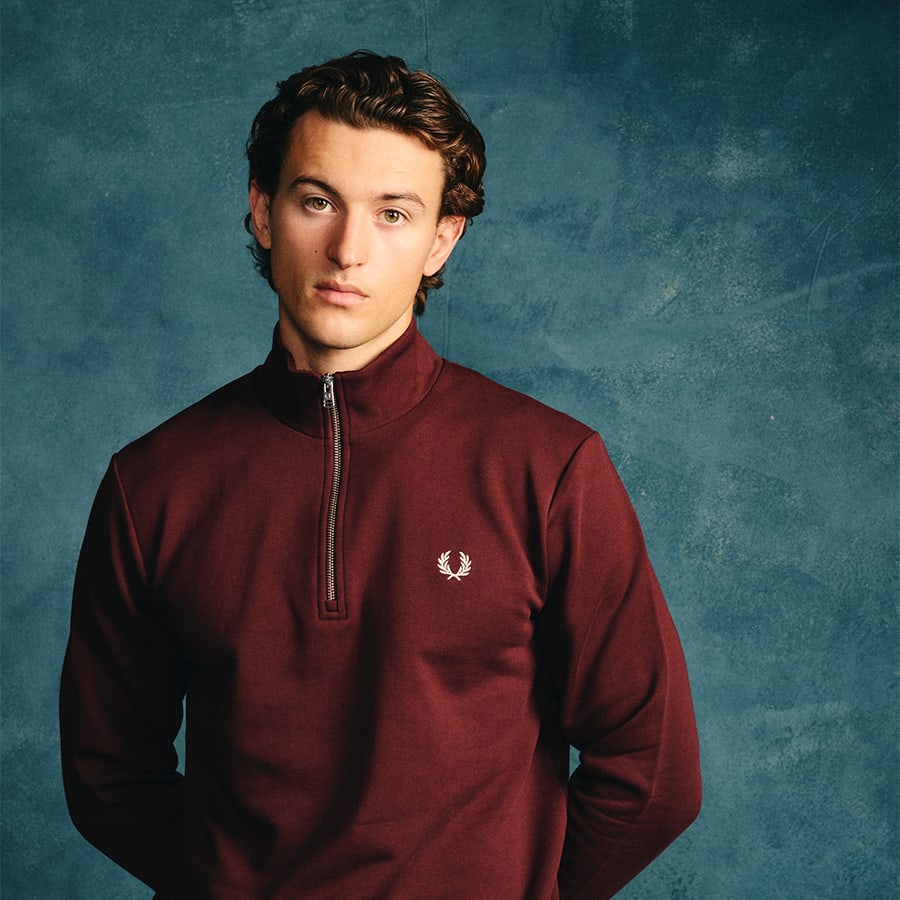 A man dressed in a burgundy quarter-zip Fred Perry sweatshirt
