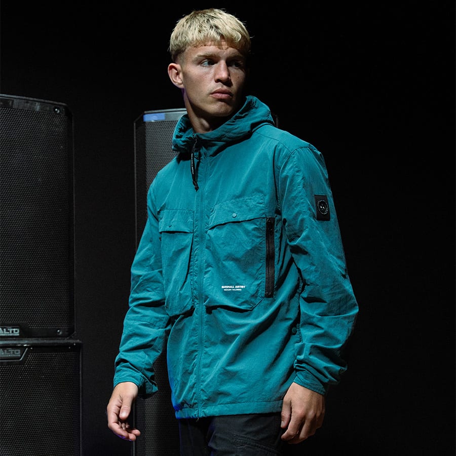 A man standing in a dark room wearing a Marshall Artist coat